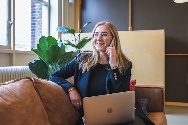 A smiling lady on the phone with blond hair and reading glasses.